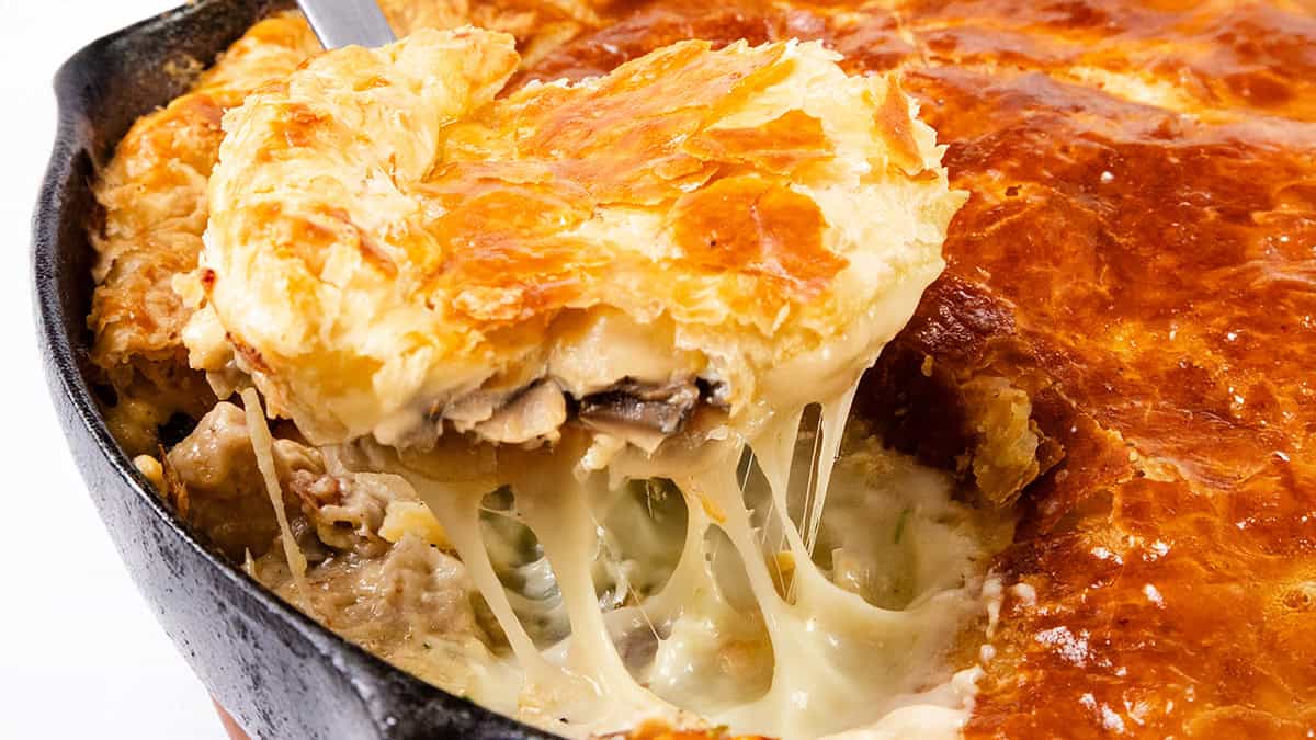 A close-up of a freshly baked pot pie in a skillet. A portion has been cut and lifted, revealing gooey melted cheese, flaky golden-brown crust, and creamy mushroom filling that rivals even the best chicken cutlet recipes in comfort and flavor.