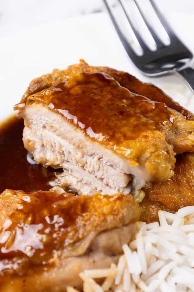 Close-up of a serving of crispy skin chicken thighs with rich bourbon glaze, accompanied by a side of white rice. A fork is placed on the plate, partially visible in the background.