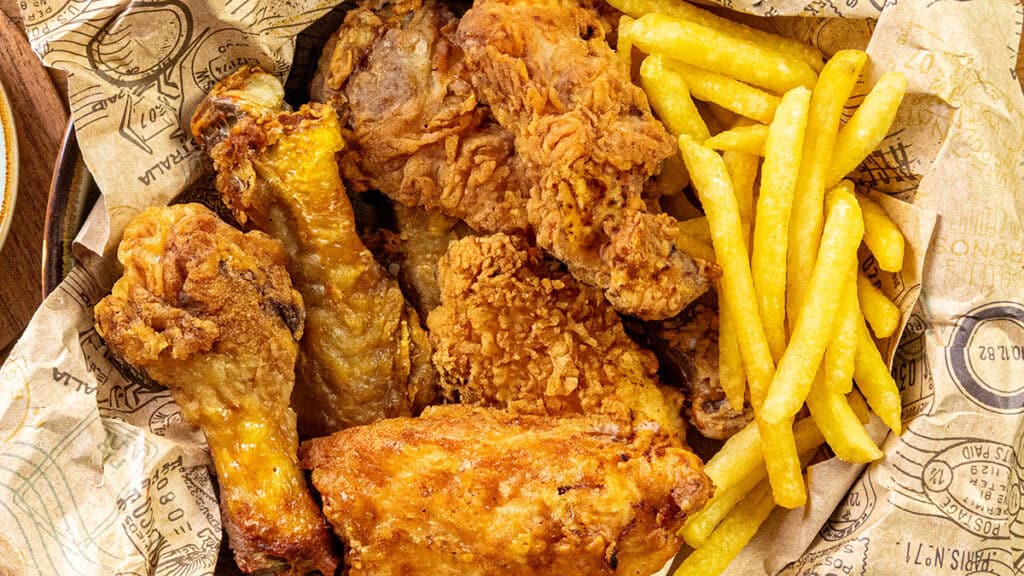 A basket filled with crispy fried chicken pieces, reminiscent of the finest chicken cutlet recipes, and golden French fries on patterned paper.