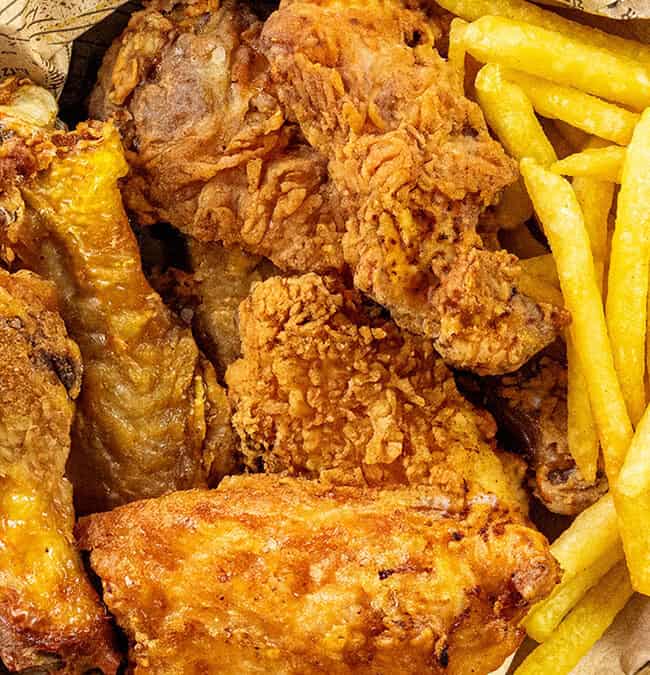 A basket filled with crispy fried chicken pieces, reminiscent of the finest chicken cutlet recipes, and golden French fries on patterned paper.