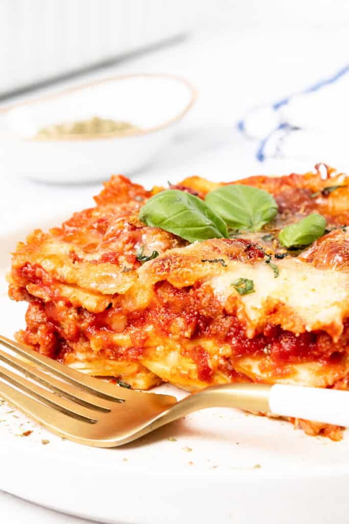 A slice of Italian Sausage Ravioli Casserole topped with a fresh basil leaf sits on a white plate.