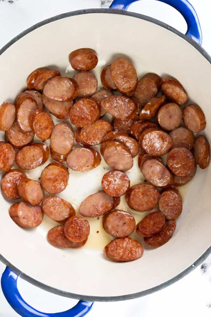 Sliced sausages frying in a white and blue enamel pot. 