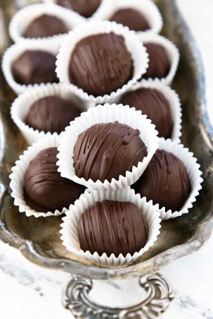 A tray of decadent Oreo truffles in white paper cups. Each truffle is topped with a drizzle of chocolate, revealing a delightful Oreo dessert underneath. The ornate tray handle complements the surface, which features a subtle white marble pattern.