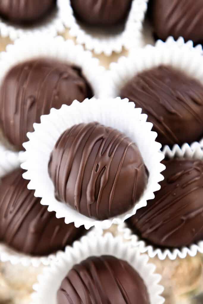 Close-up of several Oreo truffles in white paper cups, their smooth surfaces adorned with chocolate drizzles creating a textured pattern. The focus is on one central truffle, with others slightly blurred in the background, enhancing their delicious allure.