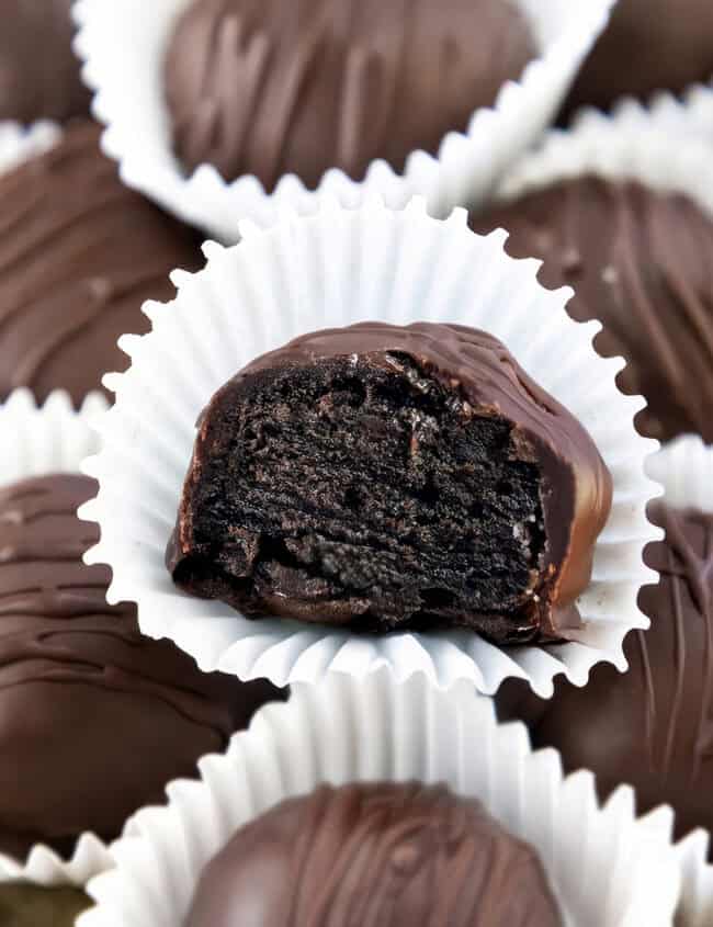 A close-up of Oreo chocolate truffles, each in a white paper cup. The focus is on one truffle with a bite taken out, revealing a rich, dark chocolate filling. Other whole truffles are blurred in the background, showcasing this delightful dessert's allure.