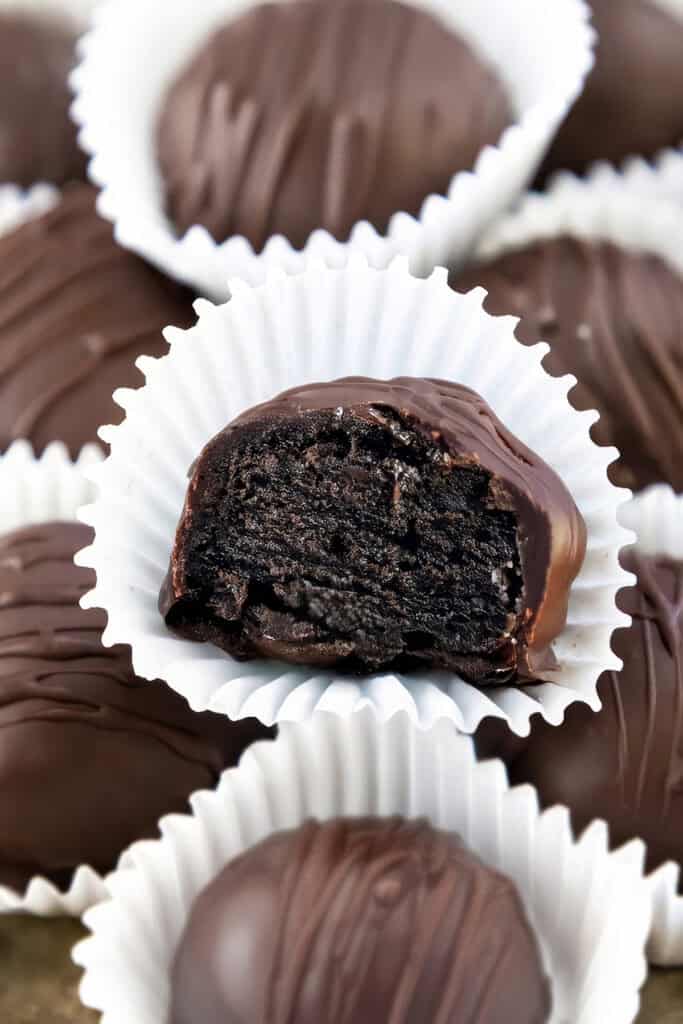 A close-up of Oreo chocolate truffles, each in a white paper cup. The focus is on one truffle with a bite taken out, revealing a rich, dark chocolate filling. Other whole truffles are blurred in the background, showcasing this delightful dessert's allure.