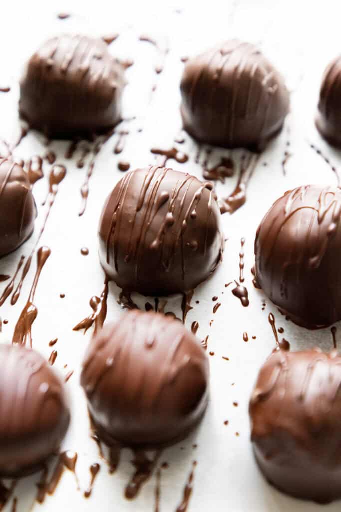 Close-up of chocolate-covered truffles arranged on a white surface. The treats are round, with a smooth coating of chocolate and additional Oreo drizzles on top, creating a textured pattern.