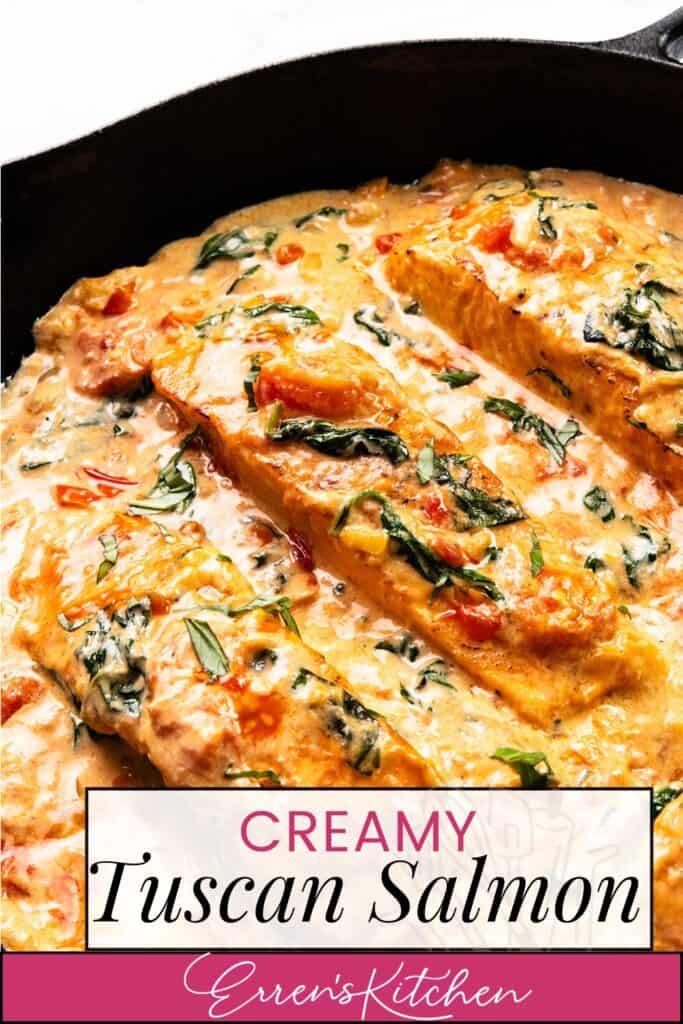 A skillet of Tuscan salmon showcases salmon fillets in a creamy sauce with spinach, tomatoes, and herbs. The dish is richly flavored and topped with fresh ingredients, beautifully displayed on a white background. "Creamy Tuscan Salmon - Erren's Kitchen" adds the final touch.