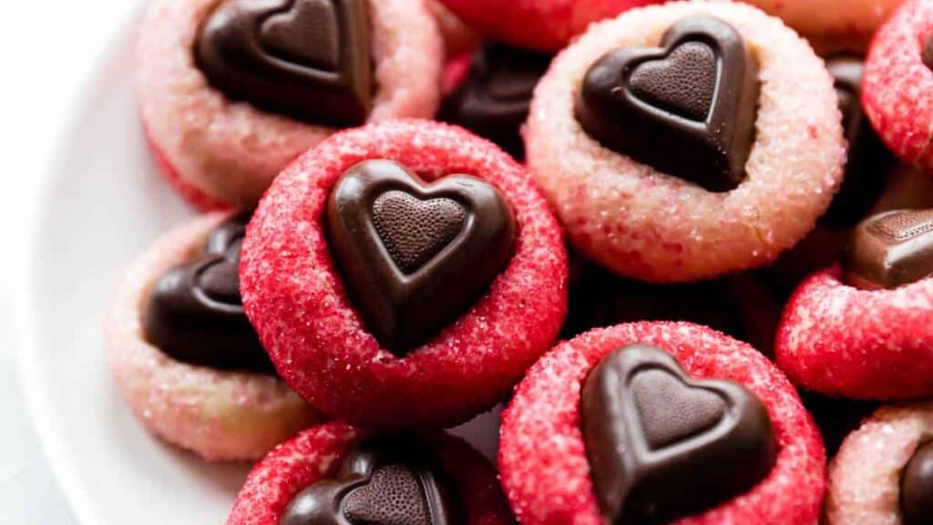 A plate of heart-shaped chocolate cookies with red and pink sugar coatings, perfect as Valentine's treats. The cookies are arranged closely, showcasing their decorative chocolate centers against a white plate—an ideal way to say "I love you" in every sweet bite.