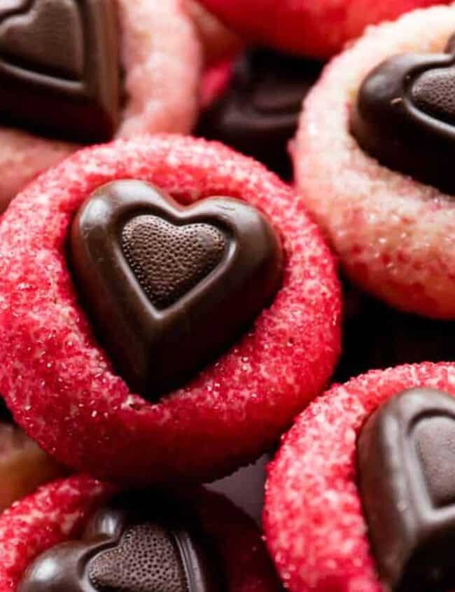 A plate of heart-shaped chocolate cookies with red and pink sugar coatings, perfect as Valentine's treats. The cookies are arranged closely, showcasing their decorative chocolate centers against a white plate—an ideal way to say "I love you" in every sweet bite.