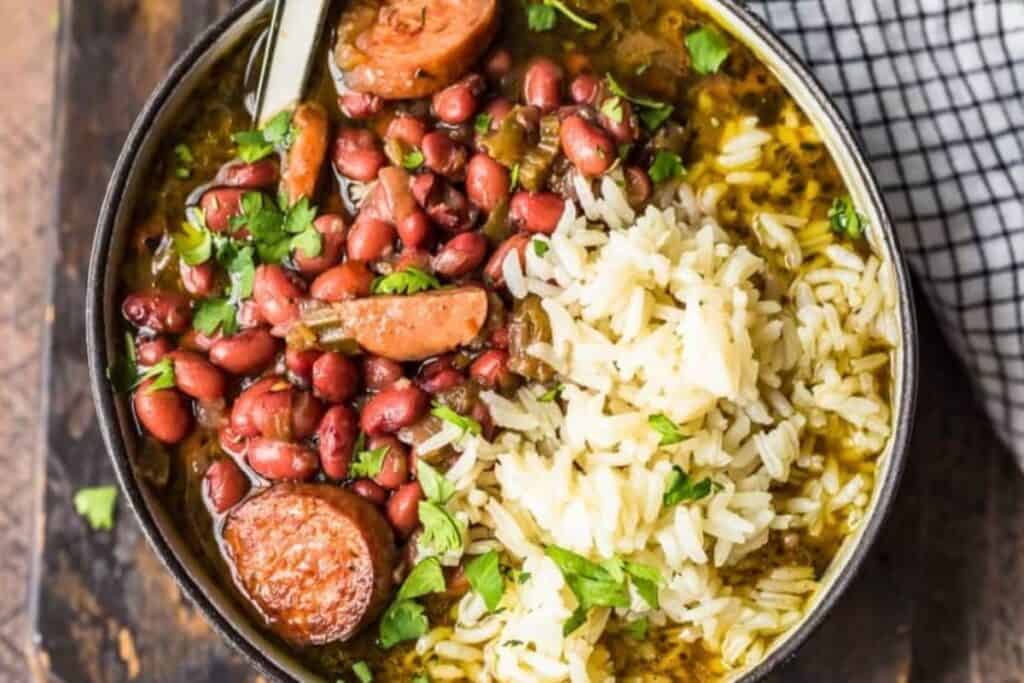 A bowl brimming with Southern flavors—red beans, sausage slices, and white rice—garnished with fresh parsley. A spoon rests in the bowl, inviting you to savor this classic Southern recipe. A black and white checkered cloth adds a touch of charm to the scene.