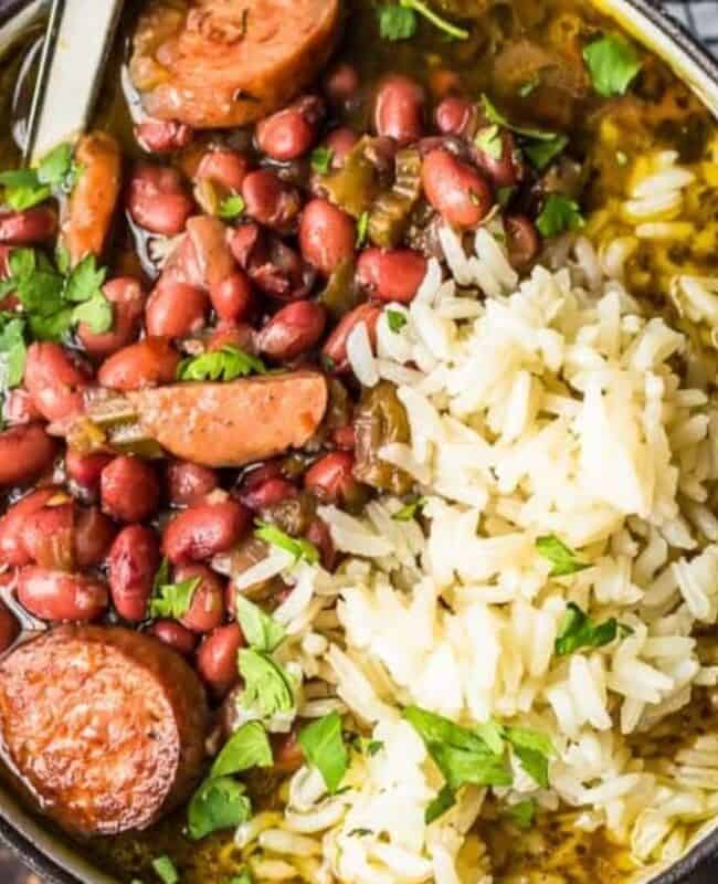 A bowl brimming with Southern flavors—red beans, sausage slices, and white rice—garnished with fresh parsley. A spoon rests in the bowl, inviting you to savor this classic Southern recipe. A black and white checkered cloth adds a touch of charm to the scene.