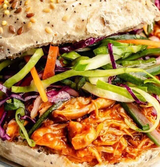 This delightful sandwich features shredded BBQ chicken, cooked to perfection in a slow cooker, and topped with a colorful slaw of green and purple cabbage, carrots, and cucumbers. All served on a seeded bun, the vibrant toppings bring a fresh, crunchy texture to the dish.