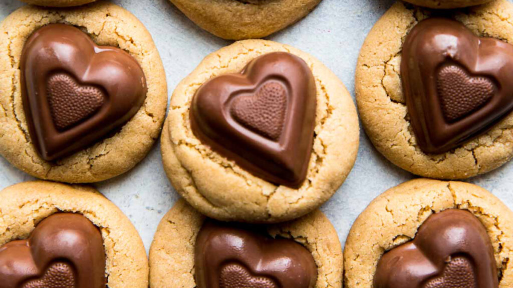 A close-up of several heart-shaped chocolate cookies with peanut butter bases. Perfect treats for Valentine's Day, each cookie features a molded chocolate heart on top, showcasing rich textures and a warm, inviting color palette.