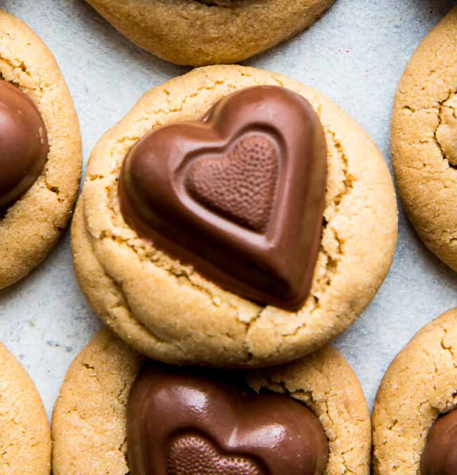 A close-up of several heart-shaped chocolate cookies with peanut butter bases. Perfect treats for Valentine's Day, each cookie features a molded chocolate heart on top, showcasing rich textures and a warm, inviting color palette.