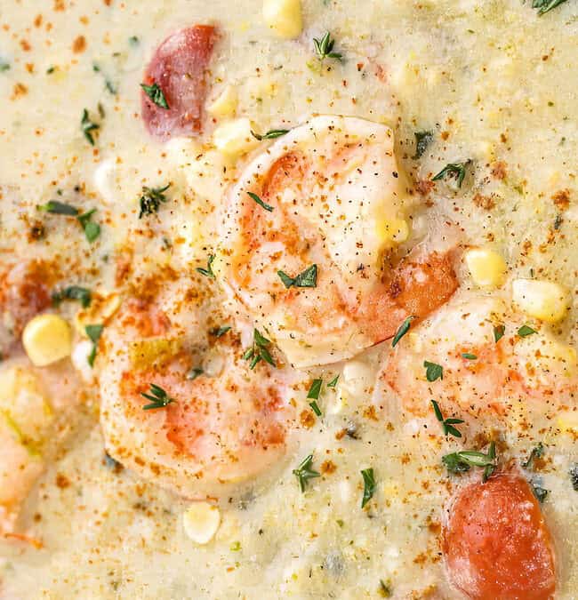 A creamy shrimp chowder, inspired by Southern cuisine, is garnished with fresh herbs and paprika. The dish boasts pieces of shrimp, corn, and potatoes, creating a rich, colorful appearance with a hint of warm spices sprinkled on top.