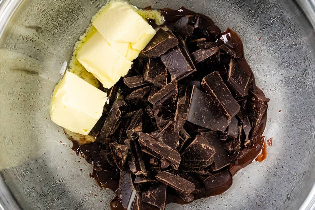 Blocks of butter and chopped dark chocolate pieces sit in a silver metal bowl, primed for melting into a decadent chocolate mousse.