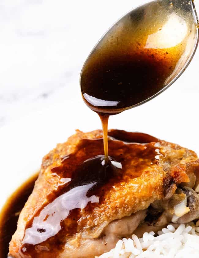 A spoon drizzles a rich bourbon glaze over crispy skin chicken thighs, perfectly paired with white rice on a plate.