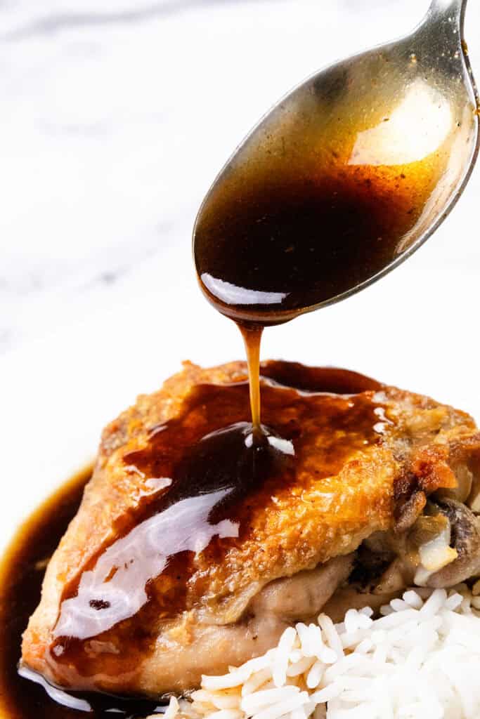 A spoon drizzles a rich bourbon glaze over crispy skin chicken thighs, perfectly paired with white rice on a plate.