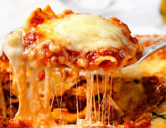 Close-up of a slice of Italian Sausage Ravioli Casserole being lifted from a dish. This classic Italian recipe boasts a rich layer of melted cheese stretching with mozzarella strands. The dish features a tomato-based sauce and hints of fresh basil on top.