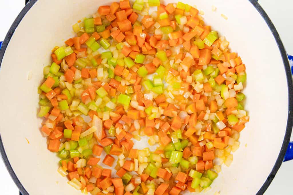 Diced carrots, celery, and onions are being sautéed in a large pot for an authentic Pasta Fagioli, a staple of Veneta cuisine. The vegetables are evenly spread and appear to be lightly cooked.