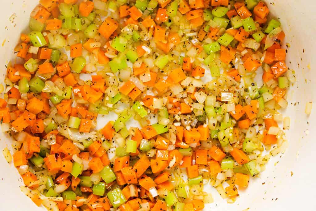 Diced carrots, celery, and onions are sautéing in a light-colored pan.