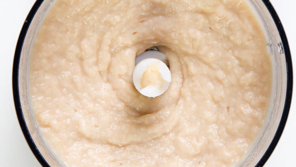 Close-up of a food processor blending a creamy mixture of beans.