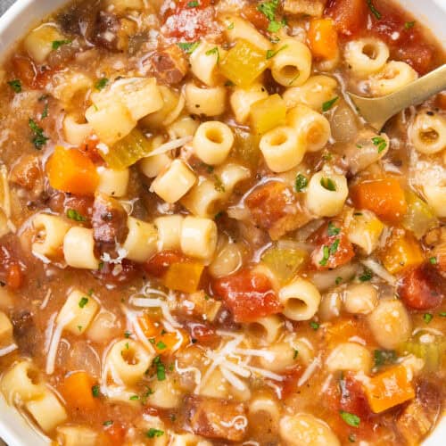 A bowl of Pasta Fagioli alla Veneta soup filled with pasta, diced tomatoes, carrots, beans, and celery, garnished with grated cheese and parsley. This classic dish of Italian cuisine boasts a hearty, rustic appearance with a variety of vibrant colors.