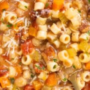 A bowl of Pasta Fagioli alla Veneta soup brimming with ditalini pasta, reminiscent of Pasta Fagioli, featuring diced vegetables like carrots and celery, hearty beans, and chunks of tomatoes. The comforting dish is garnished with Parmesan cheese and fresh herbs.