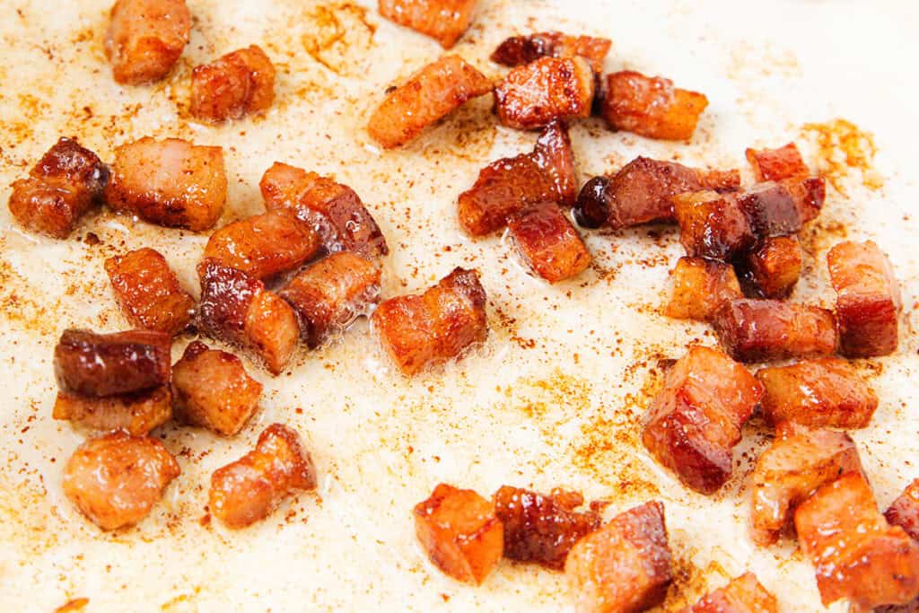 Close-up of crispy, golden brown cubes of cooked pancetta on a white surface,