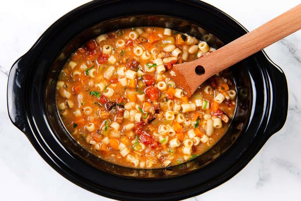 A black slow cooker filled with a hearty Pasta Fagioli alla Veneta.