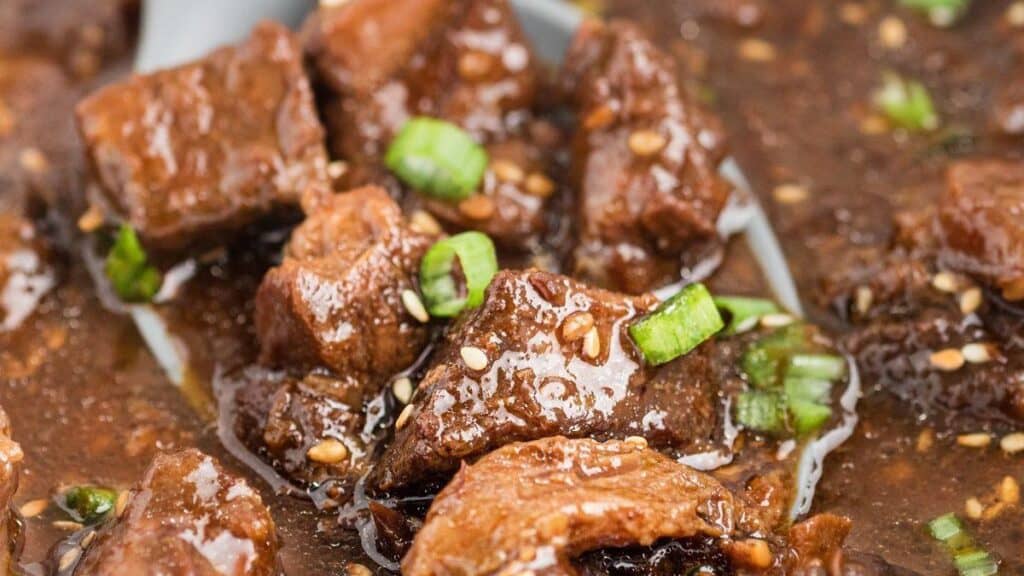 A close-up of a savory dish featuring tender chunks of beef in a rich, dark sauce teeming with big flavors. Perfect for lazy days, the beef is garnished with sliced green onions and sesame seeds, enhancing the dish's texture and taste.