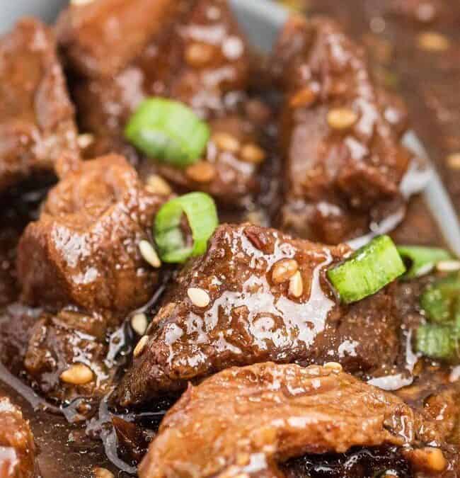 A close-up of a savory dish featuring tender chunks of beef in a rich, dark sauce teeming with big flavors. Perfect for lazy days, the beef is garnished with sliced green onions and sesame seeds, enhancing the dish's texture and taste.