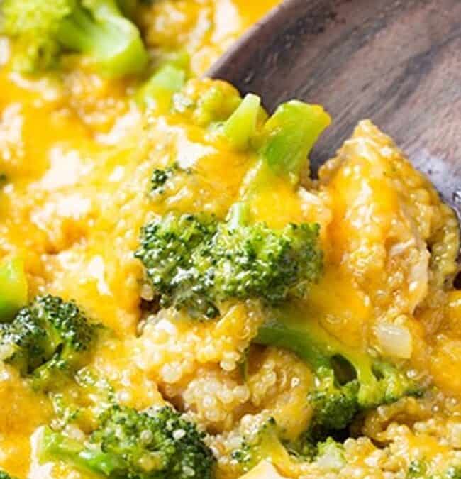 Close-up of a wooden spoon scooping creamy broccoli and quinoa casserole topped with melted cheddar cheese, perfect for an easy one-pot dinner. The dish is vibrant, with the green broccoli contrasting the yellow cheese, creating a hearty and inviting appearance.