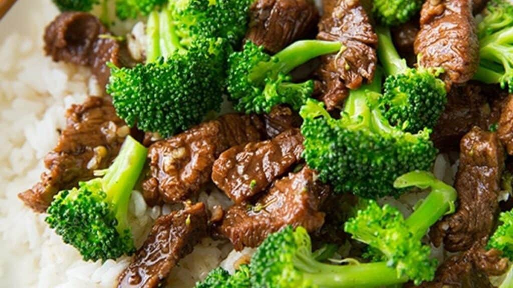 A dish featuring stir-fried beef and broccoli served over a bed of steamed white rice. The beef is cooked in a savory sauce, and the broccoli is bright green, adding freshness to the dish.